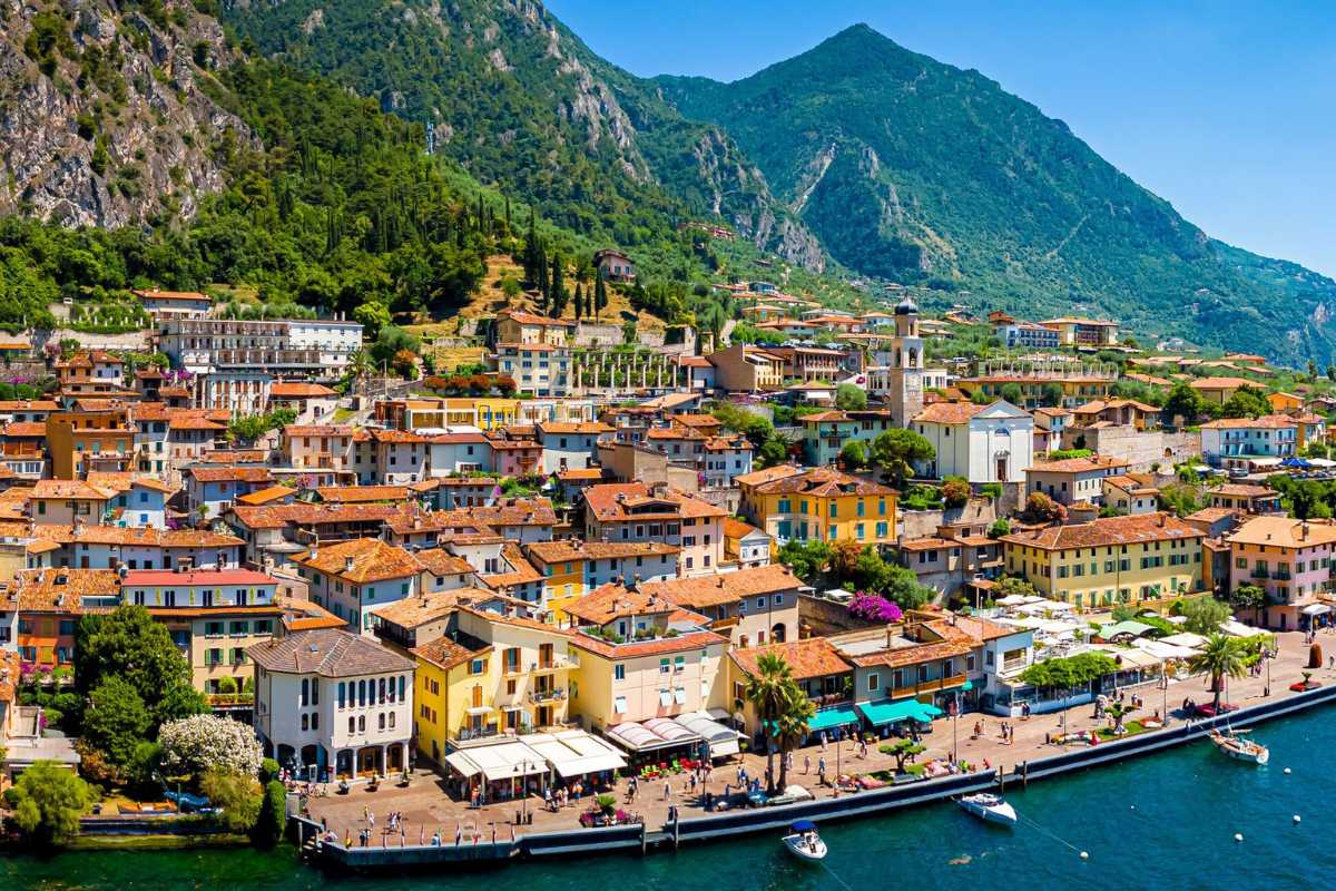 Panoramica in una giornata di sole su una delle spiagge principali di Limone sul Garda, con le montagne sullo sfondo, bagnanti e ombrelloni colorati
